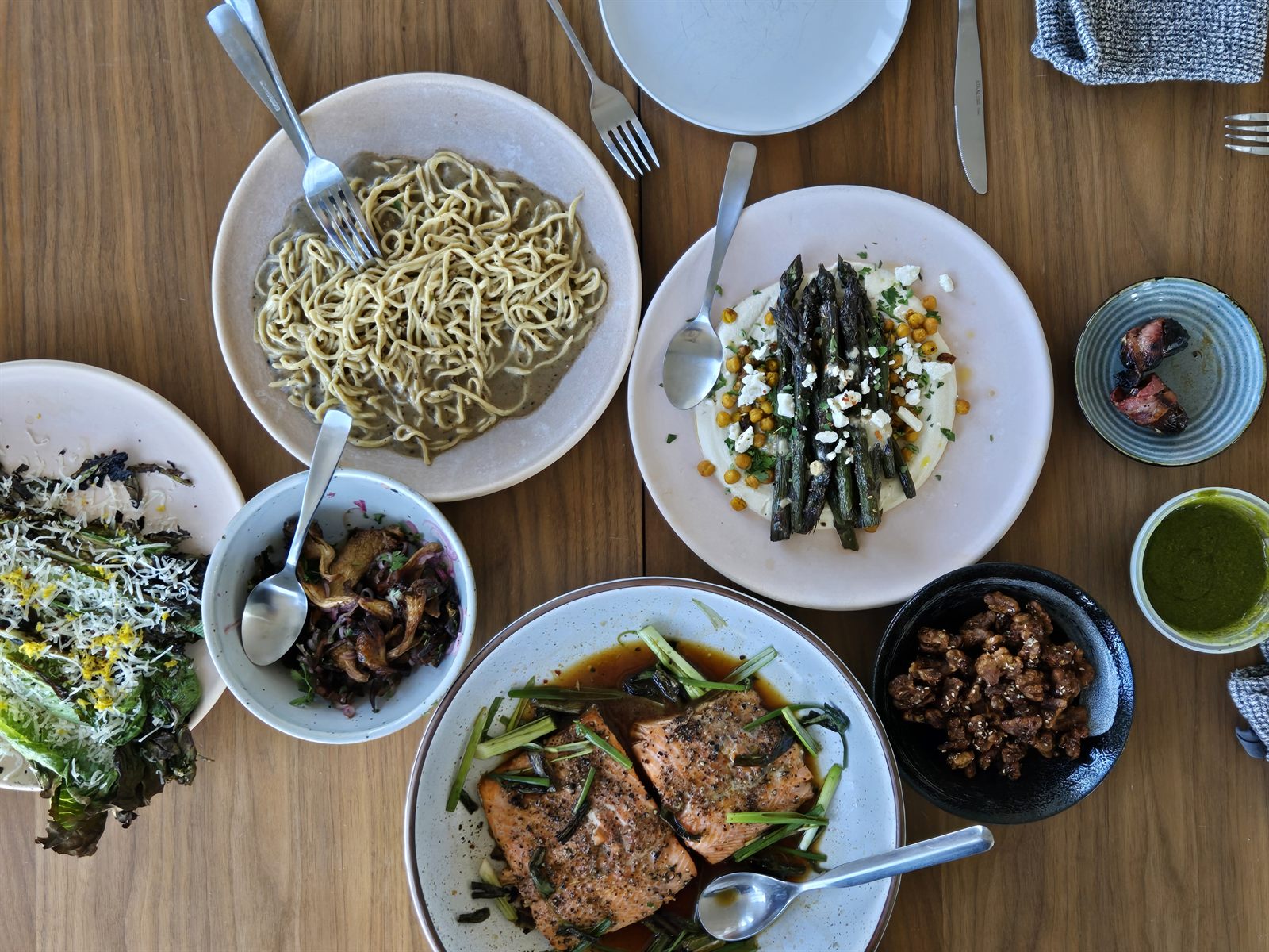 Overhead view of a table of plates — noodles, seared salmon, asparagus and sautéed mushrooms