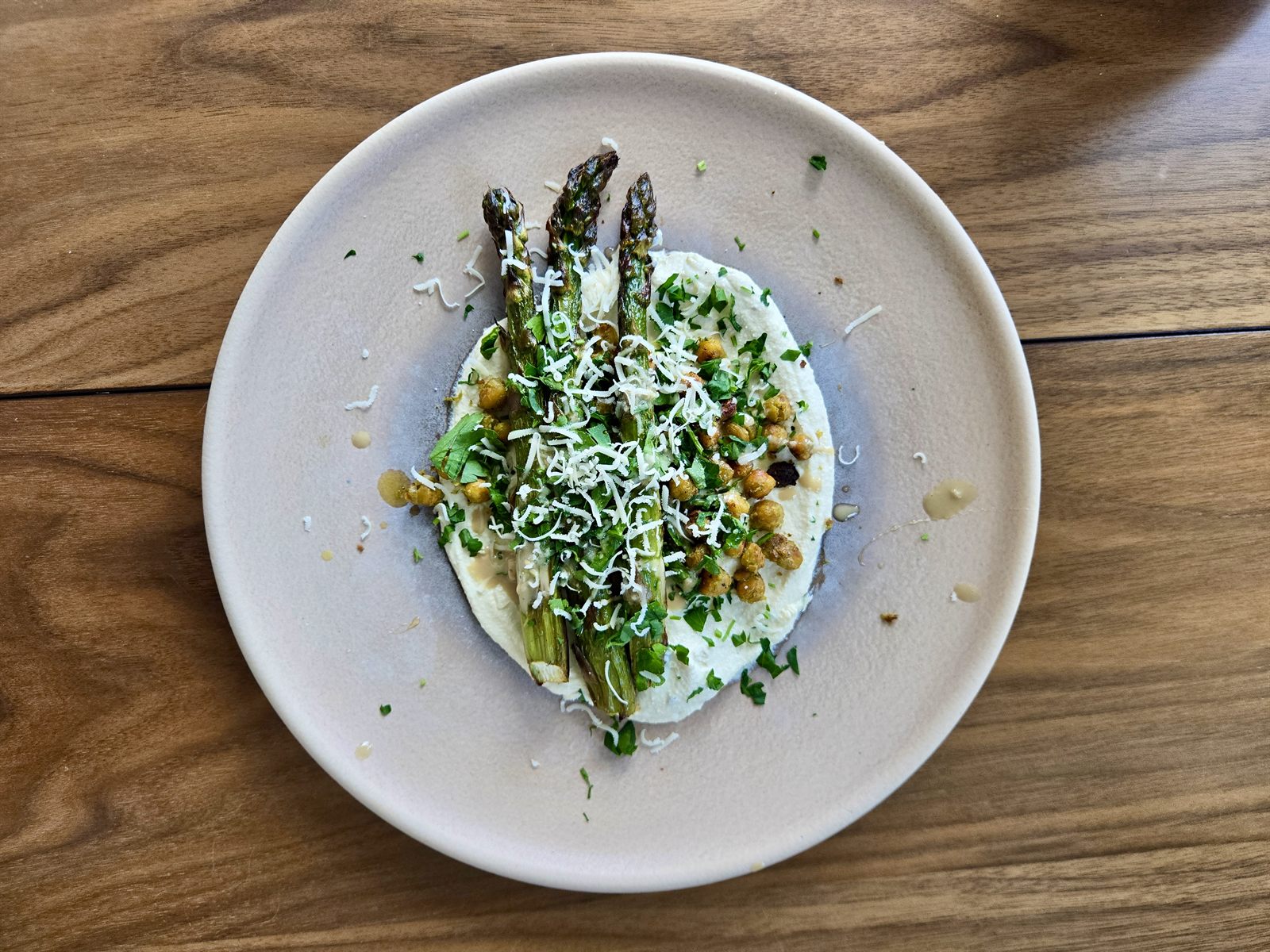 Asparagus over whipped ricotta on a white plate, finished with grated cheese
