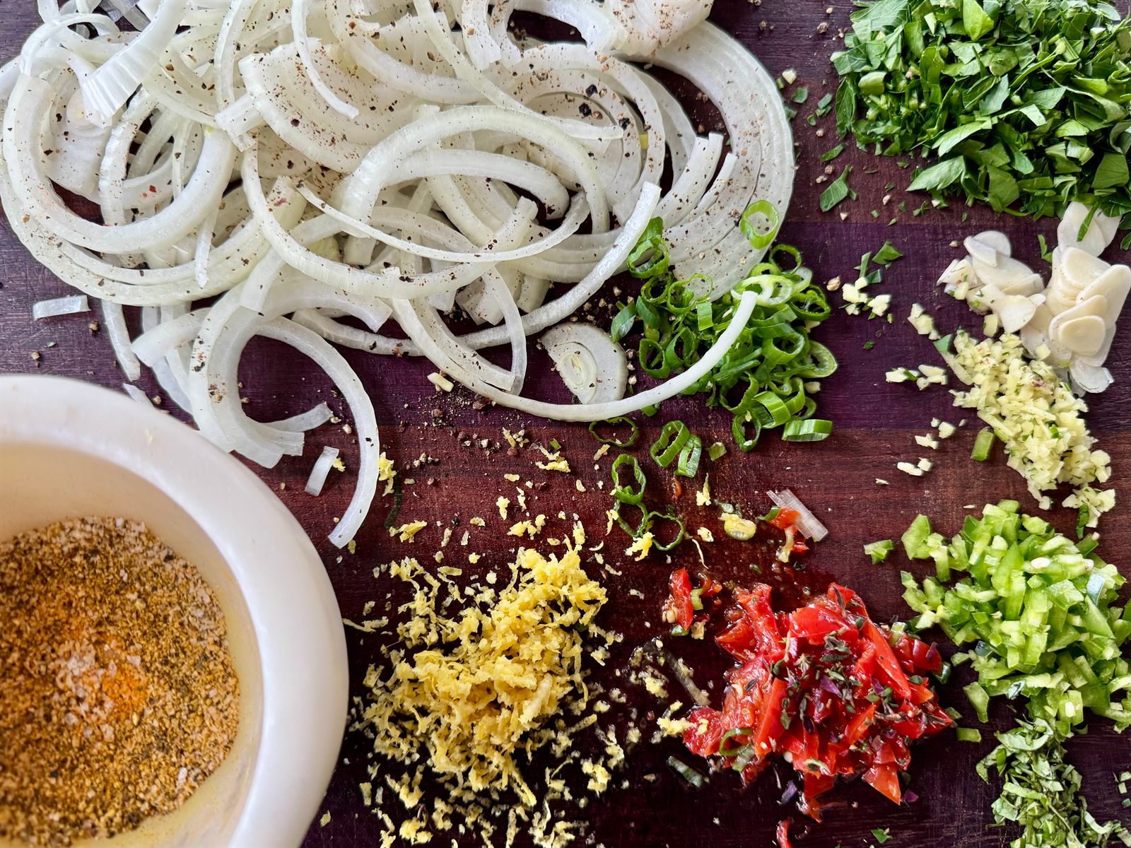 Mise en place on a board: sliced onion, chopped herbs, citrus zest, chili and spice