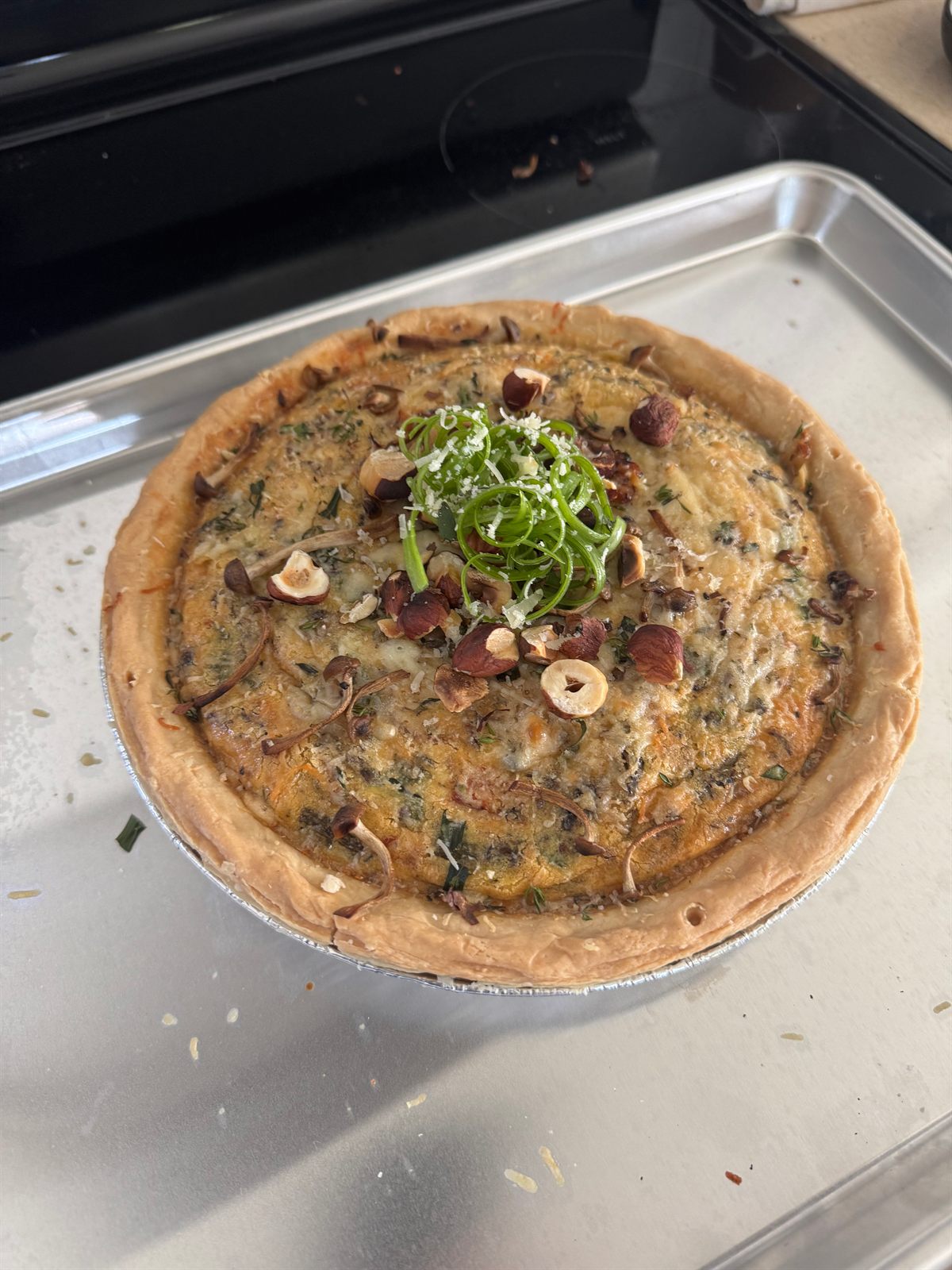 Savory tart topped with hazelnuts and green onion on a baking sheet