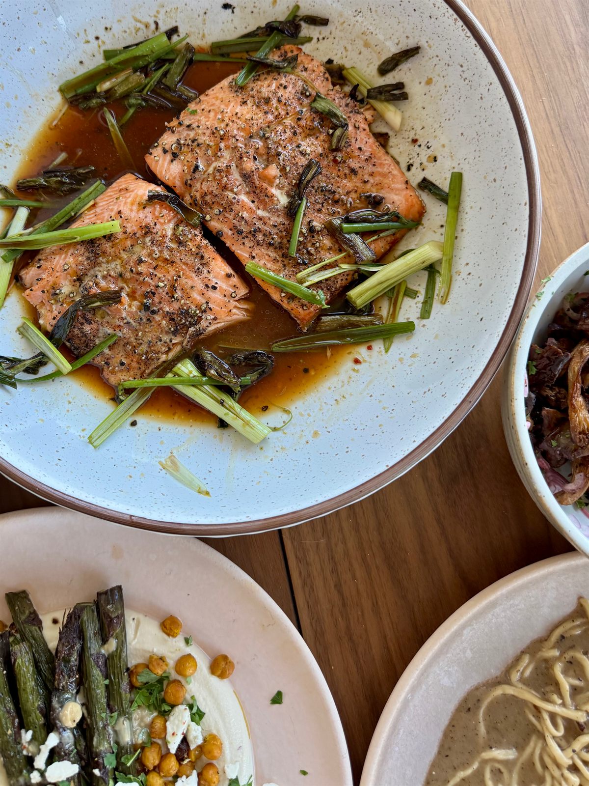 Seared salmon with a glossy sauce and scallion on a table of shared plates