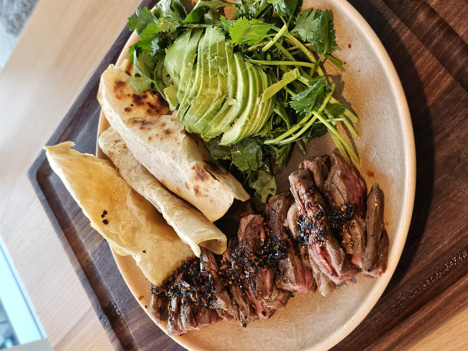 Grilled skirt steak with flatbread, avocado and arugula on a wooden board
