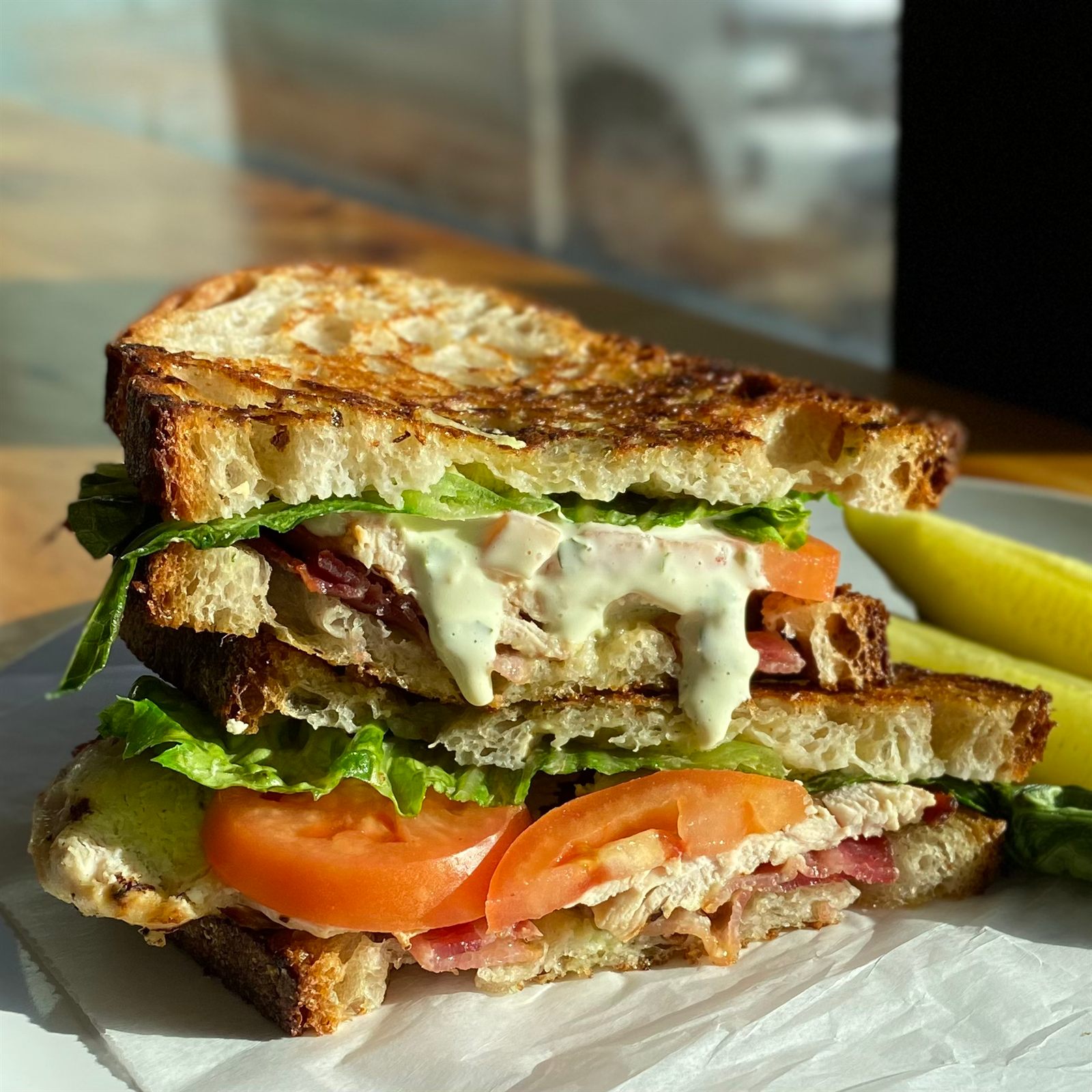 Toasted sourdough sandwich with tomato, greens, avocado-herb spread and a pickle